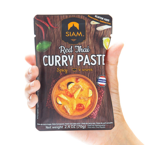 Hand holding a package of Siam Red Thai Curry Paste against a white background