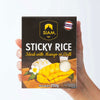 Hand holding a box of Siam Sticky Rice with mango and rice illustration on a white background